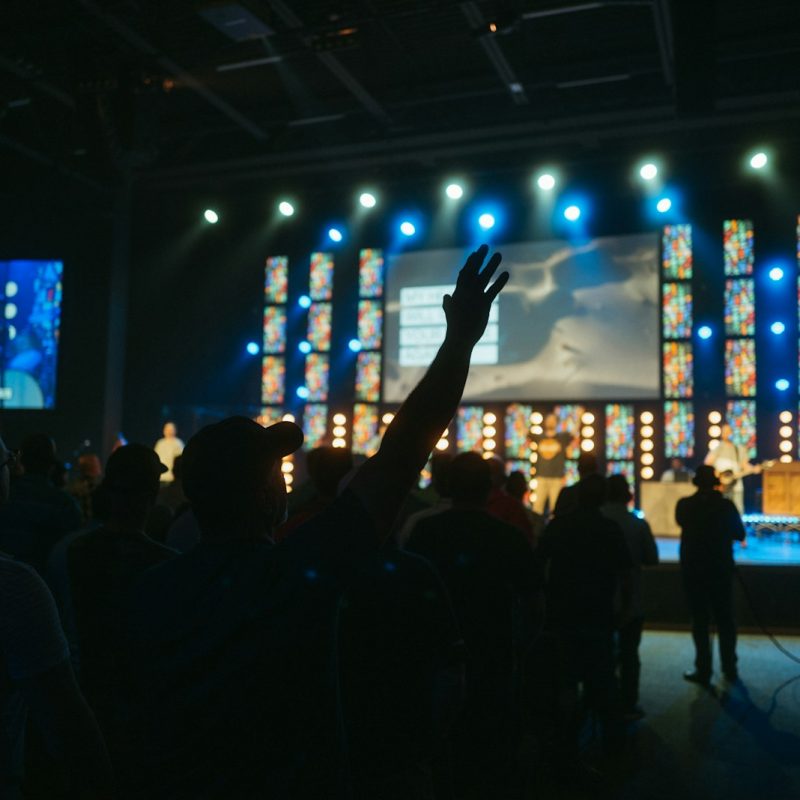 a crowd of people in a room with a stage and a large screen